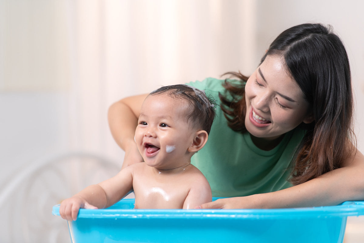 A smiling mother bathing her laughing baby in a small blue bath tub