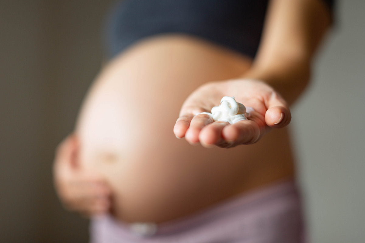 A pregnant woman smoothing lotion onto her skin